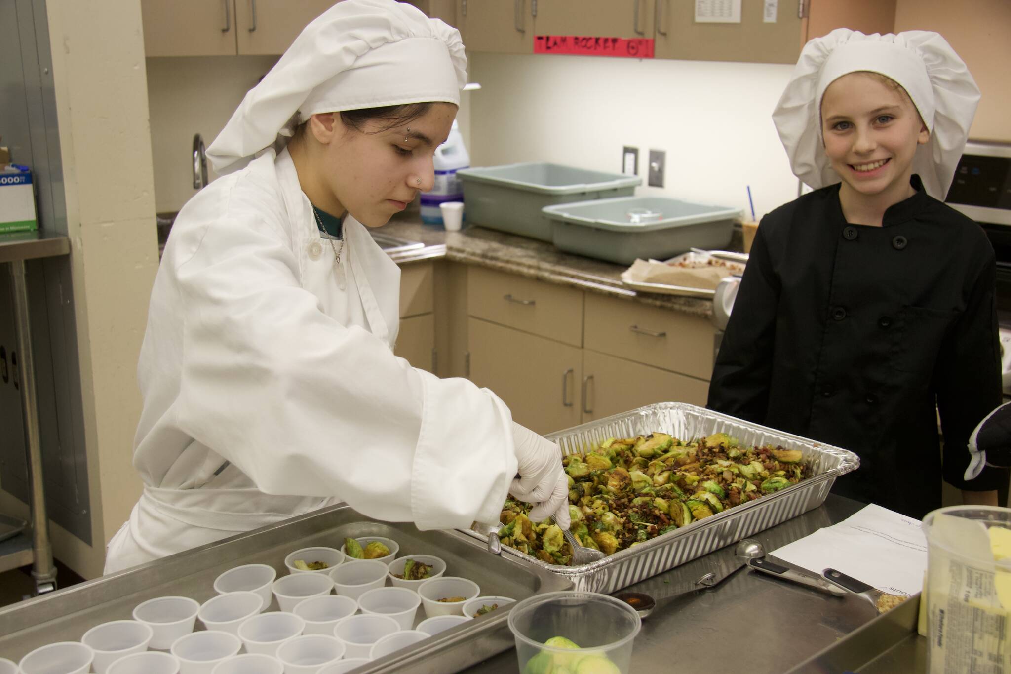 High school student Elizabeth Brennan (right) assist Madilyn Jones in preparing her Brussels sprouts dish. (Photo by Rachel Rosen/Whidbey News-Times)