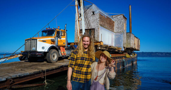 Photo by David Welton
Tevon Dubois and Chanel Jost pose in front of their house as it is loaded onto a truck at a Possession Point dock.