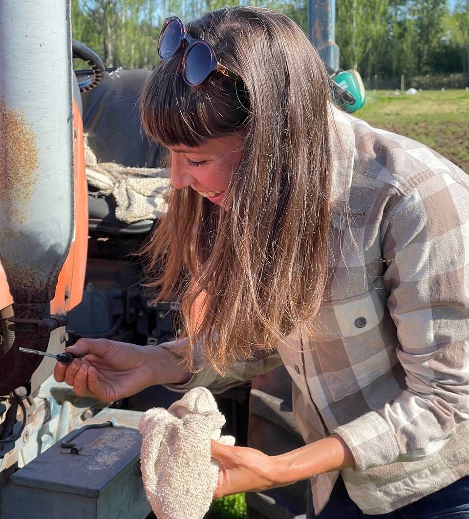 Organic Farm School student Abby Wood checks the oil on a tractor. Students learn a number of skills during the intensive program, including how to repair farm equipment. (Photo provided)