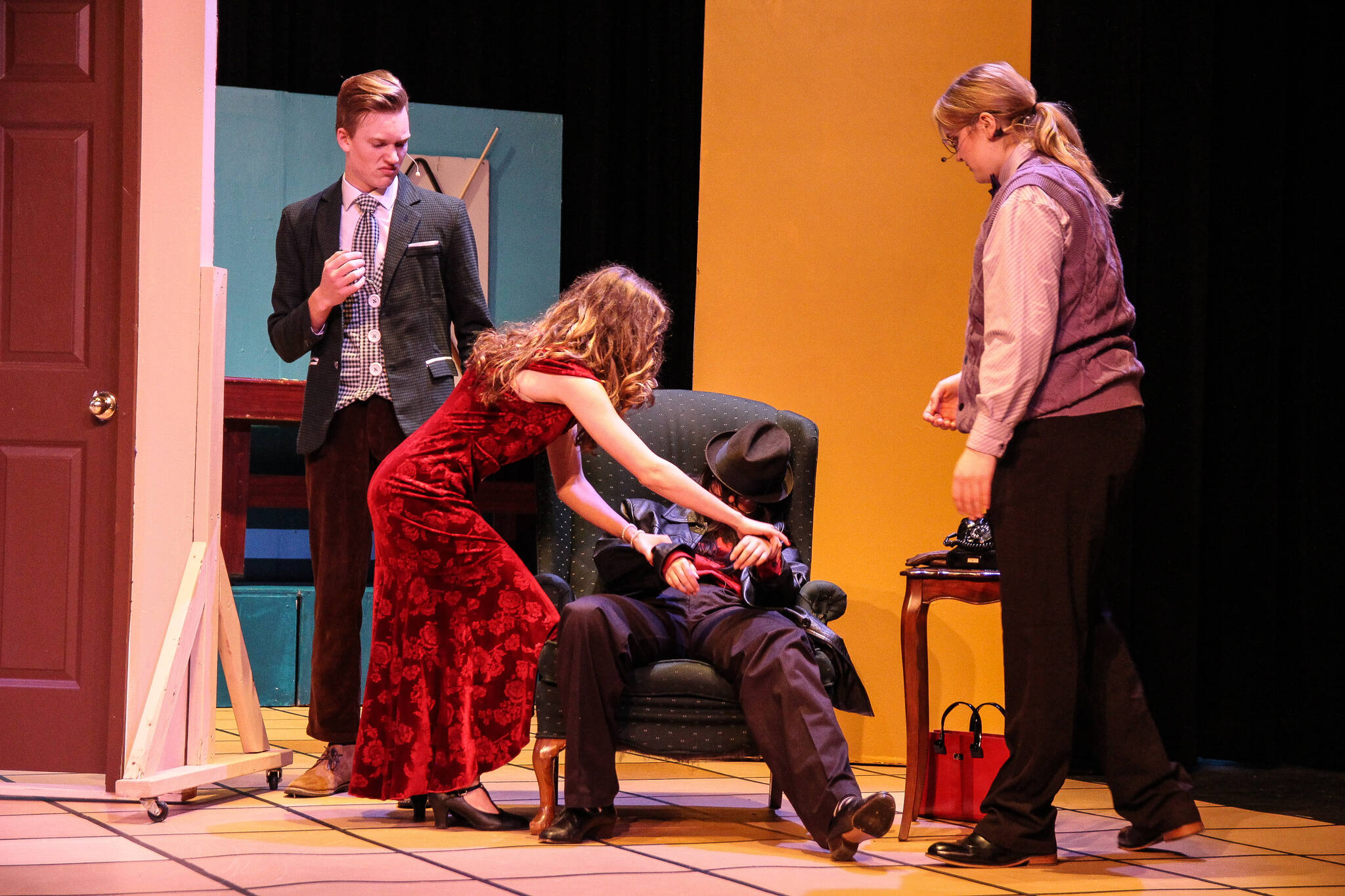Mrs. Scarlet (Isabella Barbee) tries to make the dead motorist (Alyza Doctolero) look like she’s sleeping as Mr. Green (Asher Lemme, at left) and Professor Plum (Kincaid Cochran, at right) watch. (Photo by Luisa Loi)