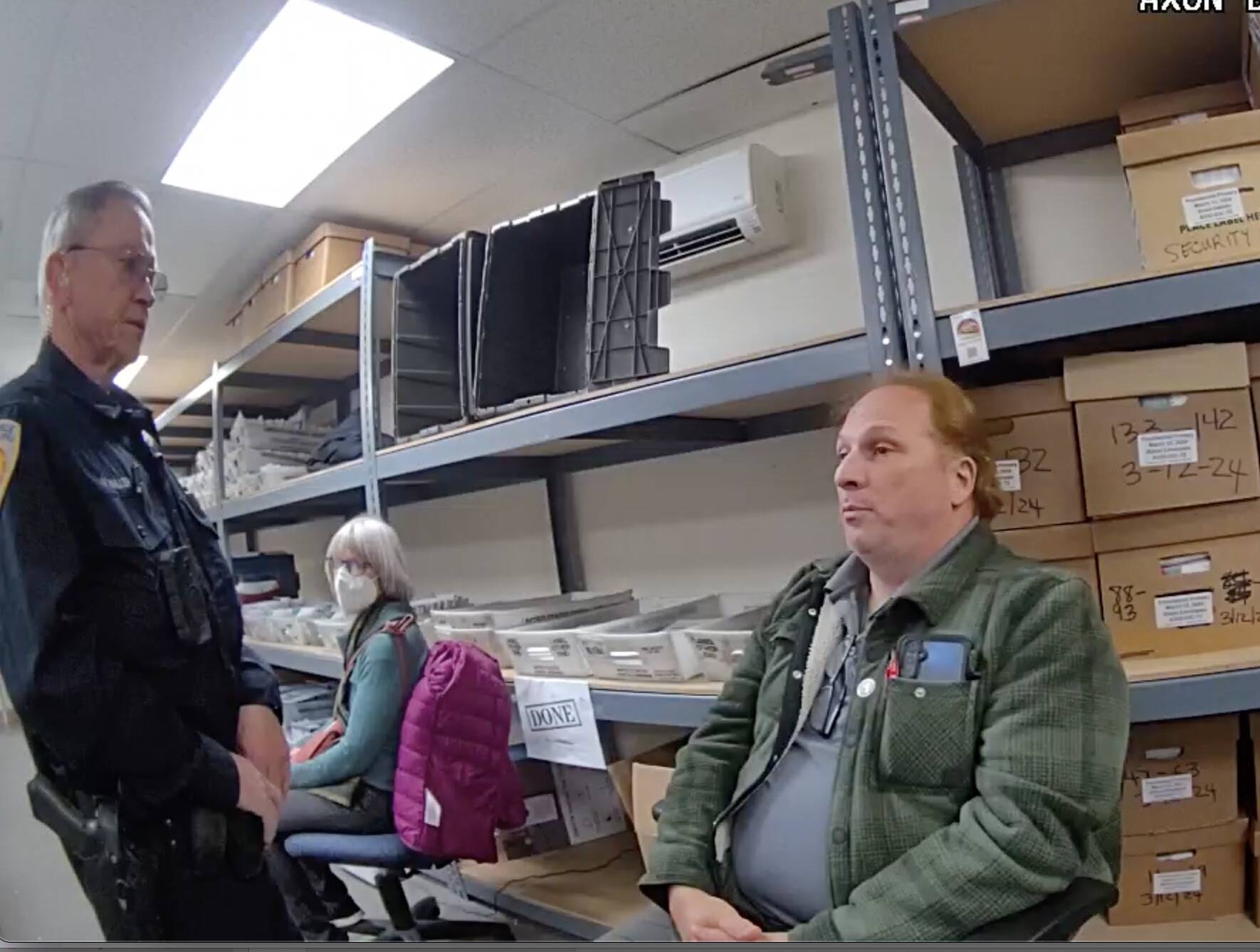A still image from a police body camera shows Timothy Hazelo with an officer in the ballot counting room.