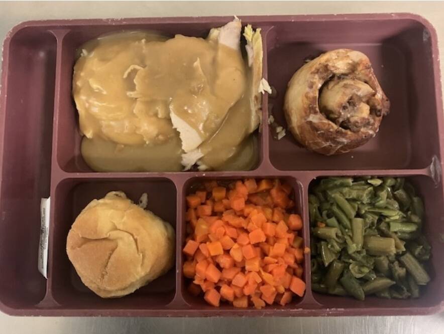 A jail meal includes turkey and gravy with mashed potato, carrot, green beans, cinnamon roll and butter garlic roll.