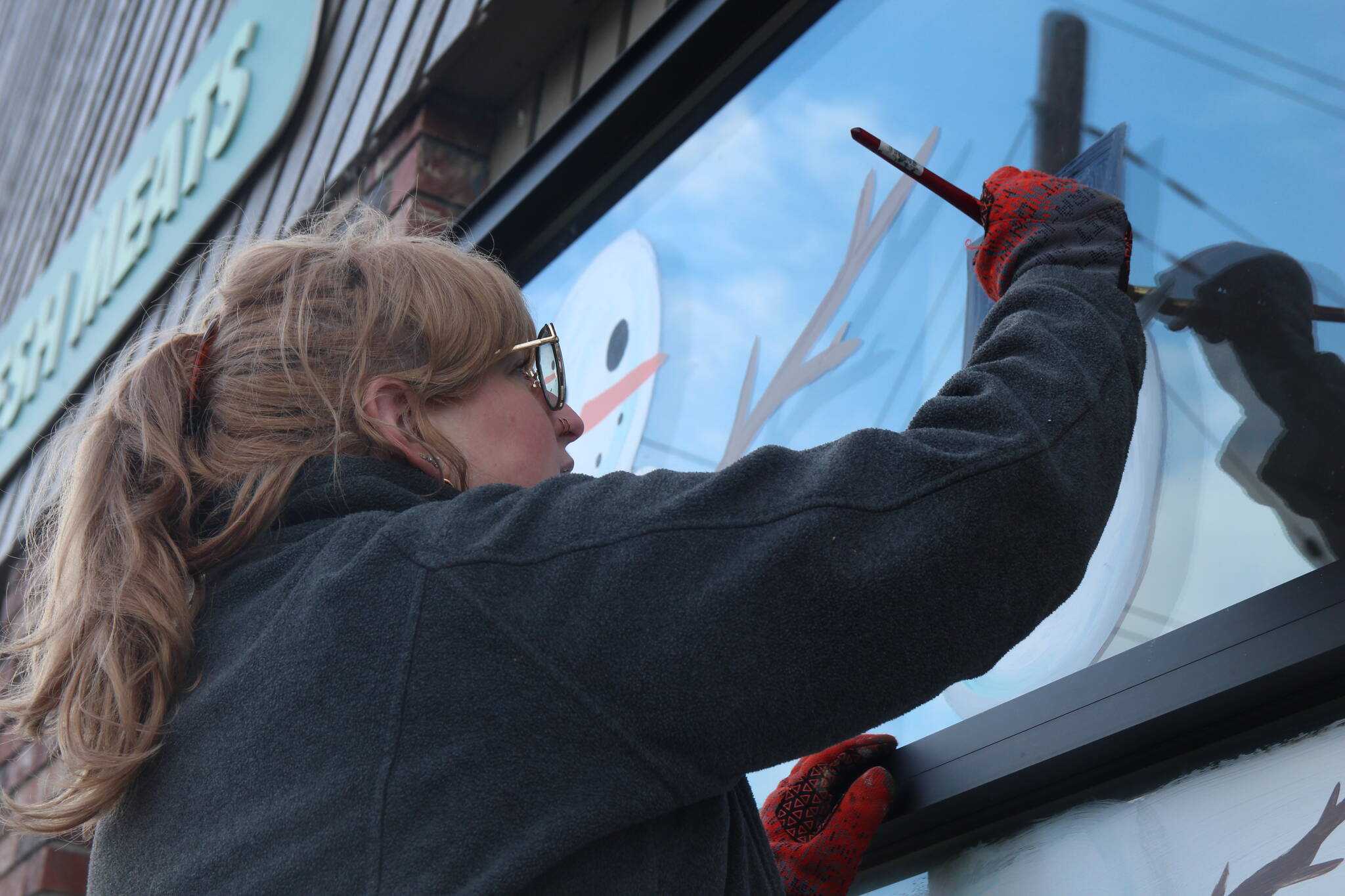 Photo by Marina Blatt. Oola Fisher paints a top hat on the Praire Center Market window in Coupeville, turning a snowman into a snowgentleman.