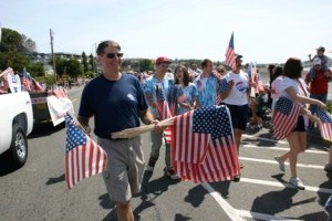 Jim Neilon of RE/MAX Acorn Properties hands out flags to parade watchers alongside Pioneer Way.