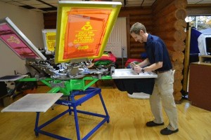 Ashley’s Design owner Eric Peterson screen prints at the shop’s new location in Trader’s Village.