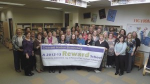 The staff of Crescent Harbor Elementary School shows a banner that highlights being named a reward school by the Office of Superintendent of Public Instruction for being in the top 10 percent of Title I schools in the state.