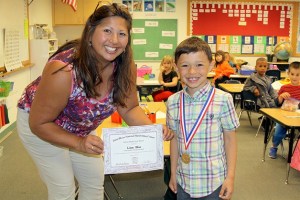 Oak Harbor Christian School kindergarten teacher Kathy Miller and student Liam Blas display a certificate and medallion awarded for his handwriting skills.