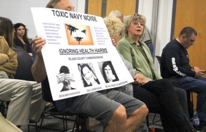 Anti-jet-noise activists hold signs at the Island County Board of Health meeting Tuesday.