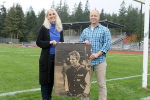 Evan Thompson / The Record Jim &ldquo;Coach&rdquo; Leierer&rsquo;s daughter, Nanette Pierson (left) and community member Jon Chapman (right) stand on South Whidbey High School&rsquo;s football field next to a picture of the deceased coach. The school board unanimously approved the stadium be renamed after longtime football coach Jim &ldquo;Coach&rdquo; Leierer on Wednesday night.