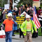 Photo by Michael B. Watkins/Whidbey News-Times                                Construction workers from WhidbeyHealth cross at State Highway 20 in Coupeville as protesters behind them protest the Dakota Access Pipeline stand outside Wells Fargo Bank in Coupeville last week. The group opposes the bank funding the pipeline project and the potential impact to the environment and native people&rsquo;s land.