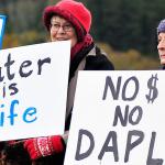Photo by Michael B. Watkins/Whidbey News-Times                                Construction workers from WhidbeyHealth cross at State Highway 20 in Coupeville as protesters behind them protest the Dakota Access Pipeline stand outside Wells Fargo Bank in Coupeville last week. The group opposes the bank funding the pipeline project and the potential impact to the environment and native people&rsquo;s land.