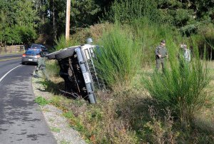 Reserve Deputy Kurt Pepper with the Island County Sheriff&rsquo;s Office speaks with a driver who rolled her Suburban onto its side Thursday on Bayview Road.