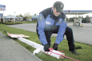 Oak Harbor Police Officer Tony Slowik removes tape Friday afternoon that was attached to a “Do Not Enter” sign by AM/PM. The sign was knocked down when a young woman lost control of her mini-van Thursday afternoon