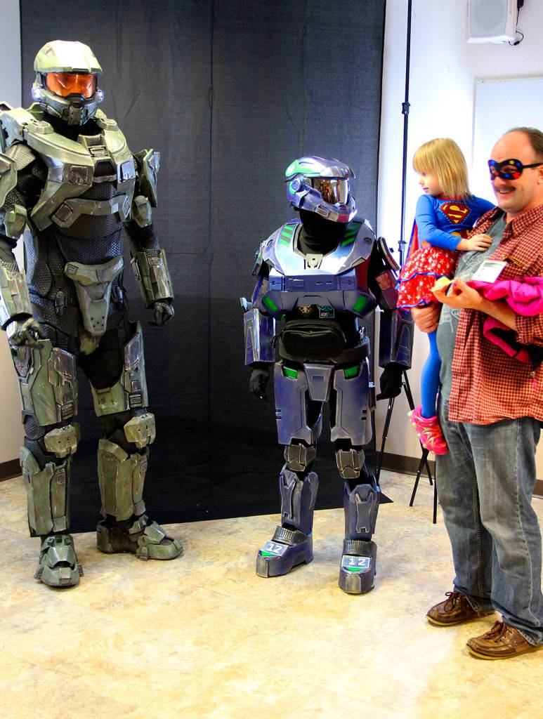 Katrina Daggett, Supergirl, held by Steve Daggett, admires Dustin Allen&rsquo;s Seahawks Master Chief armor at Oak Harbor Comicon Saturday at Oak Harbor Library. At left, Clinton resident John Groves fills out the world&rsquo;s most accurate Master Chief Armor from the Halo video game franchise. Photo by Daniel Warn/Whidbey News-Times