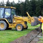 Public Works Superintendent Kelly Riepma uses a backhoe to drop dirt into a trench as public works employees Jimmy Wadlington and Scott Wofford cover a new water line going out to the community garden. Photo by Megan Hansen/Whidbey News-Times.