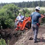 Craig Holmquist uses an excavator Monday, May 22, 2017 to dig a hole for a new vault toilet that will be installed in June near the office of Ebey&rsquo;s Landing National Historical Reserve in Coupeville. Carl Sholin, an archaeologist with the National Park Service, monitors the dig. The Reserve will be busy with several projects this summer as it braces for an increasing number of visitors. Photo by Ron Newberry/Whidbey News-Times