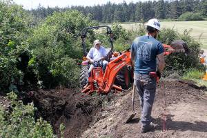 Craig Holmquist uses an excavator Monday, May 22, 2017 to dig a hole for a new vault toilet that will be installed in June near the office of Ebey&rsquo;s Landing National Historical Reserve in Coupeville. Carl Sholin, an archaeologist with the National Park Service, monitors the dig. The Reserve will be busy with several projects this summer as it braces for an increasing number of visitors. Photo by Ron Newberry/Whidbey News-Times