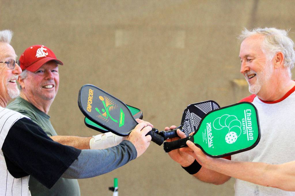After a game, players Clare Kruse, Dave Meyer, and Barry Haworth (left to right) give the customary high-five slap of their pickle ball racquets. Getting together twice a week to play pickle ball is good for friendships and fitness, say about 30 participants of the Oak Harbor Senior Center activity.