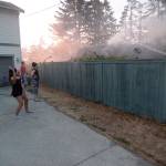 Justin Burnett/The Record &mdash; Amiee Brookhart hoses down her fence while firefighters work to extinguish a house fire next door.
