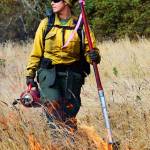 Amber Martens, of Joint Base Lewis-McChord, stands over a small section of flames from a prescribed burn that took place Thursday at Admiralty Inlet Natural Preserve. The burn is part of the Whidbey Camano Land Trust&rsquo;s effort to restore prairie lands on the island. Photo by Laura Guido/Whidbey News-Times