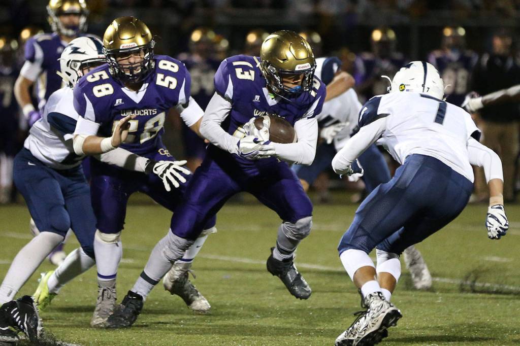 Aaron Martinez (13) picks up yardage for Oak Harbor with the help of Brandon McCollough (58).(Photo by John Fisken)
