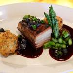 A pork belly entree with a bittersweet blueberry sauce, pickled blueberries, roasted corn fritters and charred asparagus.
