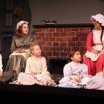 <address>Actors portraying the Cratchit children, some making their debut on stage, gather at home with Mrs. Cratchit. Left to right: Rhiannon Chapman, Gabrielle Eatonon (on stool), Ashley Coker, Ellie Collette, Diana Walker, Cheyenne Henson. </address>