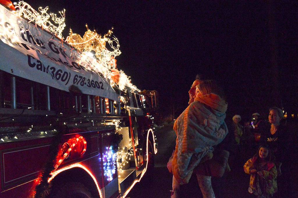 Jerry Helm holds up his daughter Scotlyn to see Central Whidbey Fires Santa. Her sister Finley and mom Lindsey also wait to greet Santa. Photo by Laura Guido/Whidbey News-Times