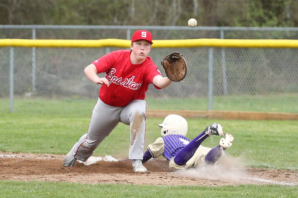 Joe Dixon slides safely into first base for an infield hit as Stanwoods Dane Carlson awaits the throw.(Photo by John Fisken)