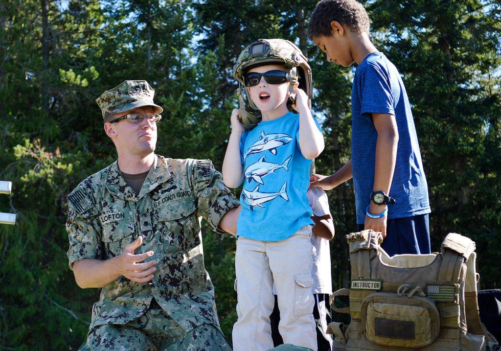 Petty Officer Nate Lofton makes sure 6-year-old Andersen Stolle doesnt fall off the Coast Guard boat as he tries on one of the helmets. The boat and equipment were one of many interactive law enforcement displays at the National Night Out Tuesday at Fort Nugent. Photo by Laura Guido/Whidbey News-Times