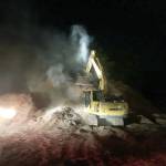 An Island County Public Works excavator spreads out a large pile of logging debris that caught fire Monday night. Photo provided