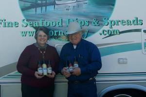 Photo by Maria Matson/Whidbey News Group.                                <em>Cornet Bay Company owners Arnie and Joanne Deckwa stand with their new seafood line of sauces. In the background, painted on their RV is the companys logo depicting Cornet Bay, the view across from their office.</em>
