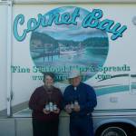 Photo by Maria Matson/Whidbey News Group.                                <em>Cornet Bay Company owners Arnie and Joanne Deckwa stand with their new seafood line of sauces. In the background, painted on their RV is the companys logo depicting Cornet Bay, the view across from their office.</em>