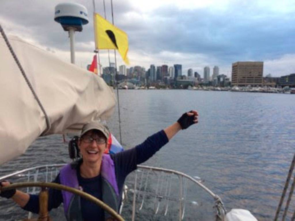 Crew member Kim Kraushar at the helm of Suva leaving the skyline of Seattle behind on the return cruise to Coupeville. The trip took one-and-one-half days each way. (Photo provided)