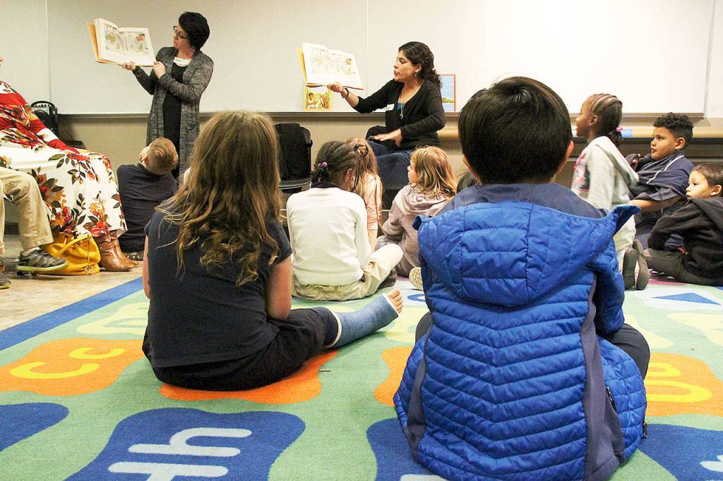 A group of third graders from Oak Harbor Elementary School listen to a story read to them by Mechelle VanHoudt, left, and Claudia Sámano Losada. Photo by Laura Guido/Whidbey News-Times