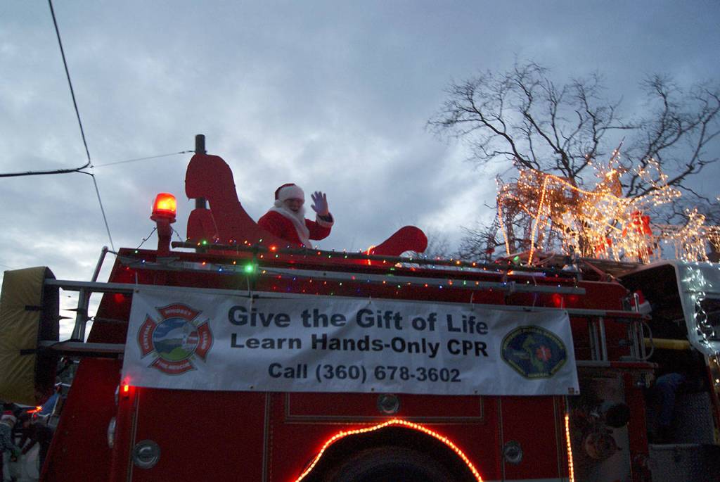 Photos by Maria Matson / Whidbey News Group.                                 Santa Claus, known as Paul Messner when off-duty, waves to the crowd on a decked-out fire truck.