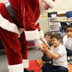 Santa gives Owen Dujmovic, a first grader in Mrs. Martins class, an orange Tuesday at Oak Harbor Elementary School. Saint Nick continued the decades-long tradition of traveling to schools in Oak Harbor to deliver the orange fruit. Photo by Laura Guido/Whidbey News-Times
