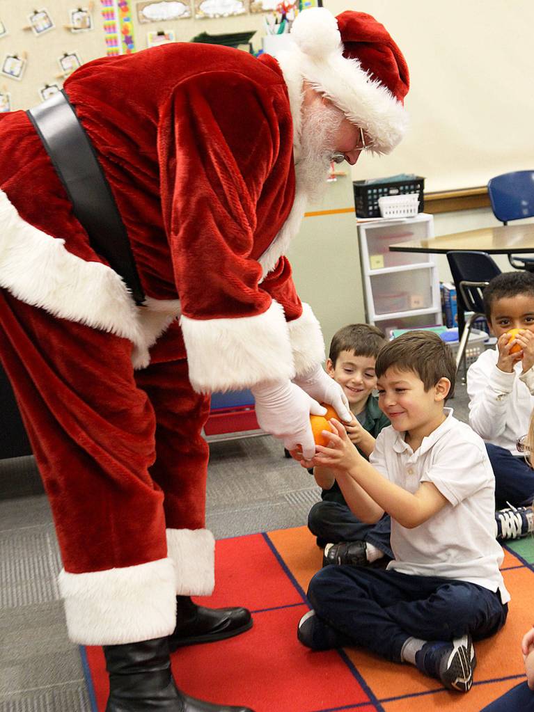 Santa gives Owen Dujmovic, a first grader in Mrs. Martins class, an orange Tuesday at Oak Harbor Elementary School. Saint Nick continued the decades-long tradition of traveling to schools in Oak Harbor to deliver the orange fruit. Photo by Laura Guido/Whidbey News-Times