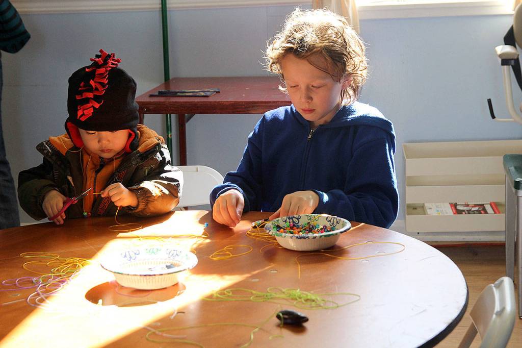 Lucas, 2, at left, and Tevian, 9, have fun Sunday creating seashell-and-bead necklaces at the childrens craft table at the Coupeville Masonic Lodge. (Photo by Maria Matson/Whidbey News -Times)