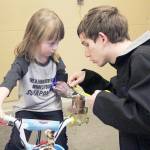 Oak Harbor High School senior Logan Ince measures an arm cuff for 4-year-old Michaela Reed to help her steer a modified bike. (Photo by Laura Guido/Whidbey News-Times)