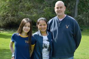 Lottery winner Brian Kutz, with daughter Kendra, left, and wife, Tuk, stand outside their Coupeville home. Photo by Laura Guido/Whidbey News-Times