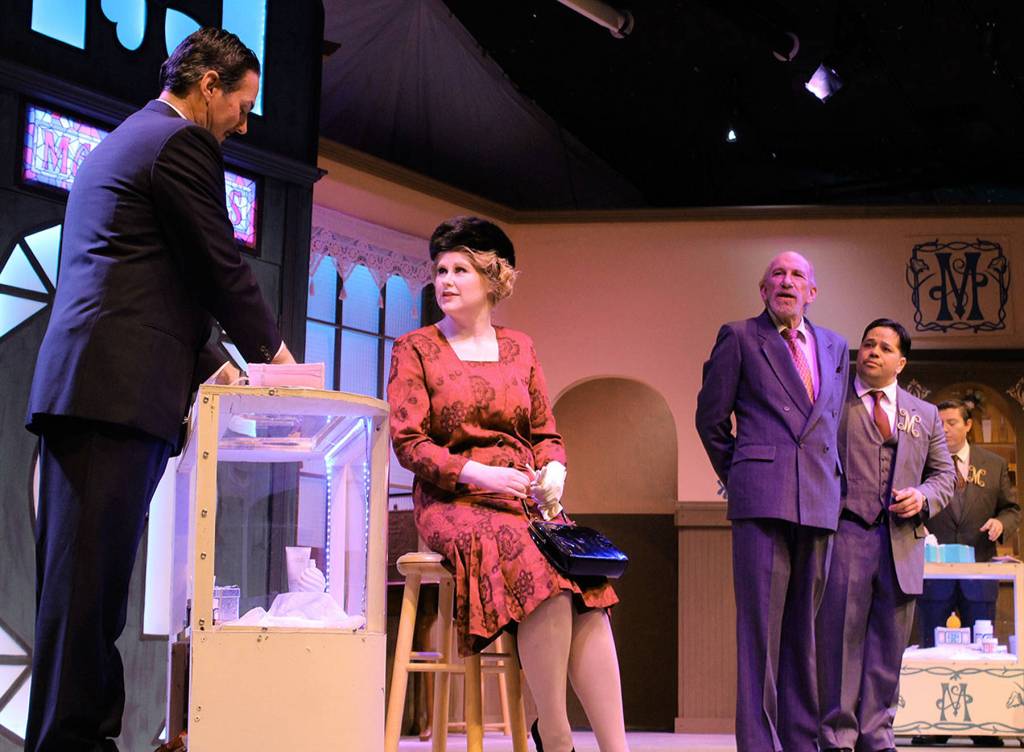 In a perfume store, salesman Steven Kodaly (Douglas Langrock) helps a customer, played by Coqui Melnick. Store owner (Kevin Wm. Meyer) and manager Georg Nowack (Karl Borja) both look on.