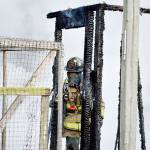 A North Whidbey Fire and Rescue firefighter walks through the remains of a chicken coop and storage building that burned down Monday morning on Penn Cove Road. Photo by Laura Guido/Whidbey News-Times