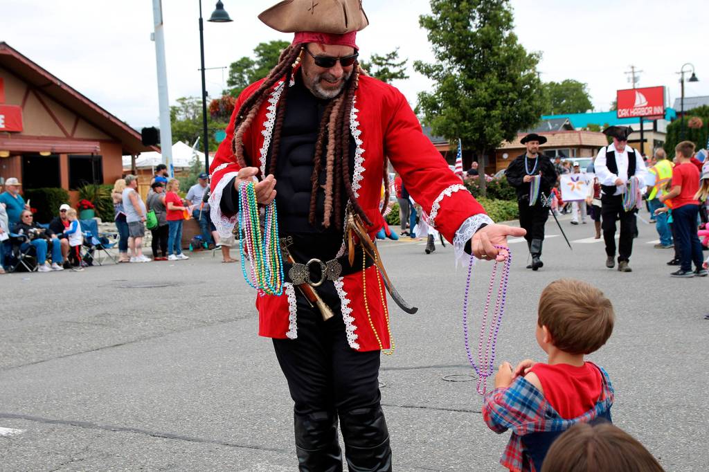 Rob Boyle of the Oak Harbor Yacht Club Buccaneers hands out beads to 3-year-old Finnigan Reilly, who was a fan of the pirate-themed parade float that made loud booms.