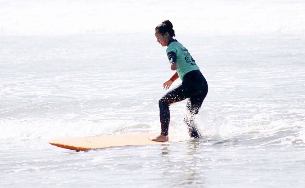 Photos by John Fisken                                Above., Jaelyn Crebbin gives surfing a try at the Beautifully-Flawed retreat. Below, Crebbin serves for the Oak Harbor volleyball team.