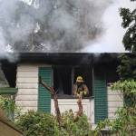 A firefighter looks out the shattered window of a home damaged by fire Friday. Photo by Laura Guido/Whidbey News-Times