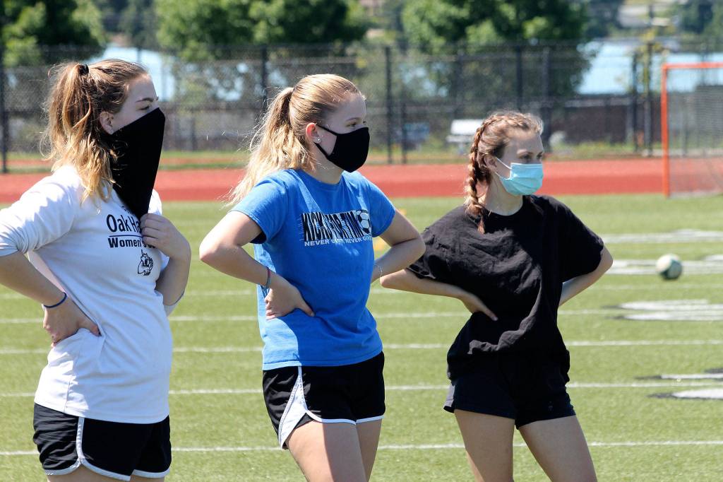 Oak Harbors Emma Erskine, left, Bailey Trease and Emily Miller listen to instructions before a drill at offseason workouts Monday. Health guidelines require athletes to wear masks when within six feet of each other. (Photo by Jim Waller/Whidbey News-Times)
