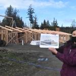 Sue Meinzinger holds up a drawing of what the Canine Condo in the background will eventually look like. There are two other buildings planned for the site. Photo by Emily Gilbert/Whidbey News-Times