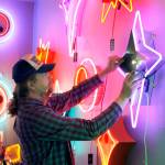 Tim Leonard, owner of the Machine Shop in Langley, hangs a purple neon star he made on the wall of his arcade. Photo by Kira Erickson/Whidbey News Group
