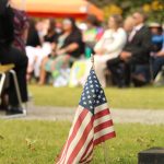 A flag marks a grave before the crowd.